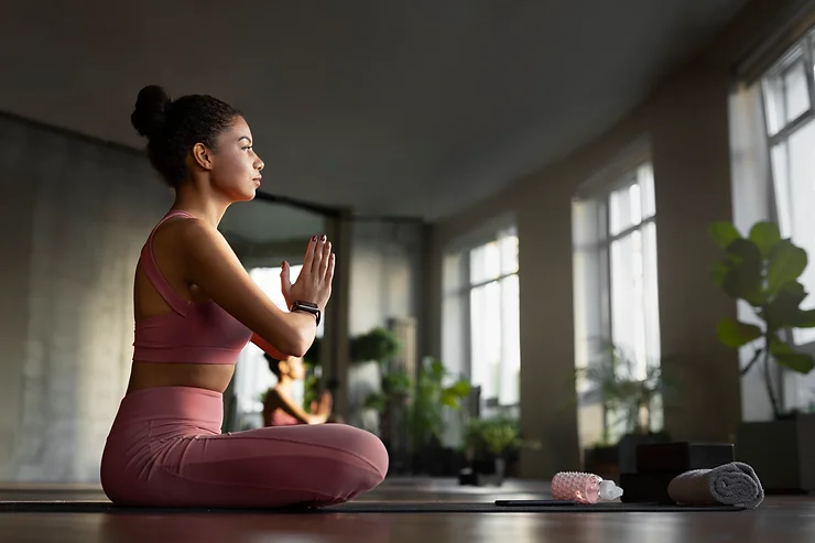 Mulher de pernas cruzadas e mãos juntas em posição de meditação.