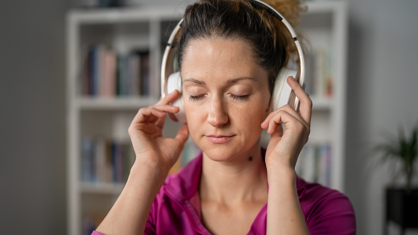 Mulher de olhos fechados e com fones de ouvido praticando meditação.