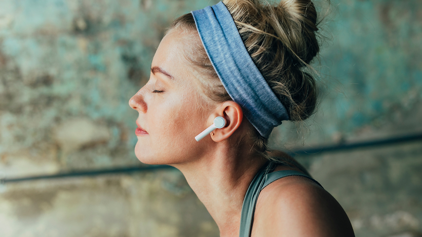 Mulher com fones de ouvido e olhos fechados praticando meditação.